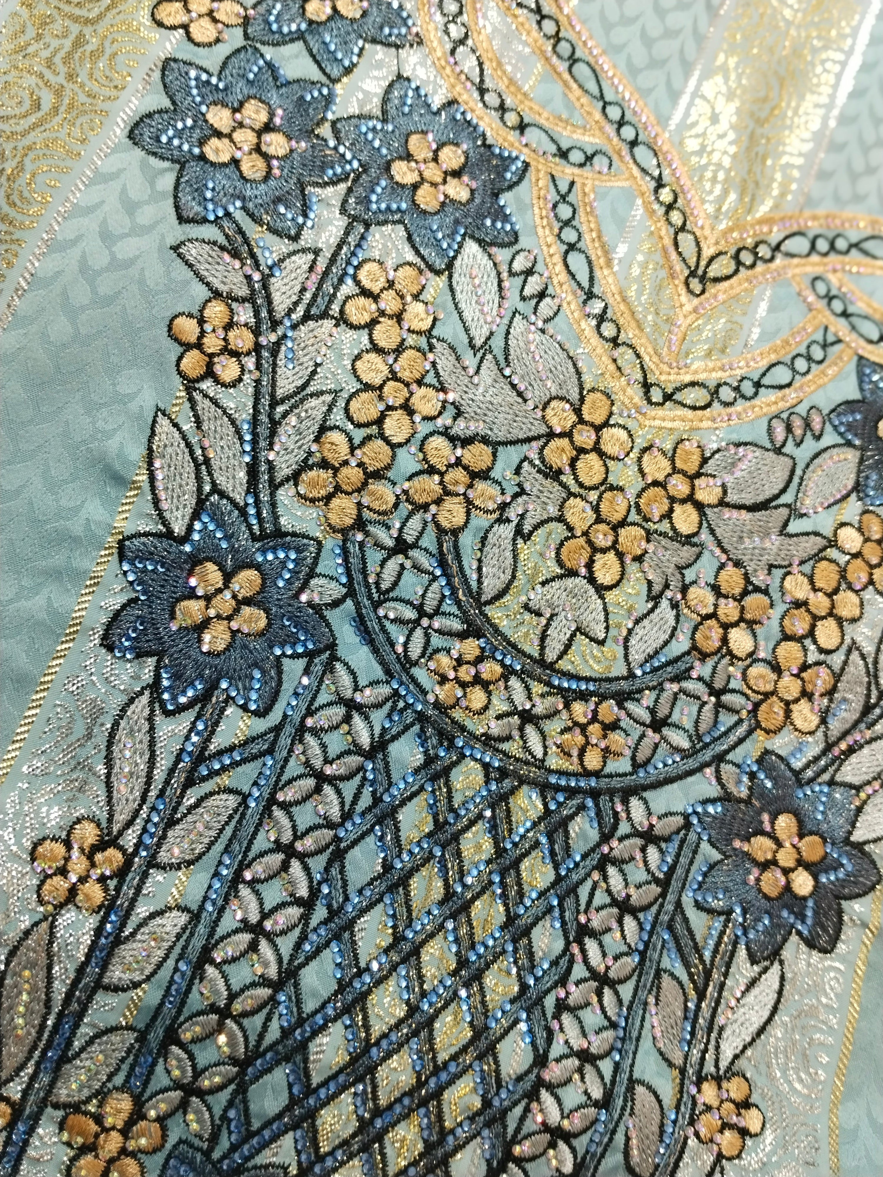 Close-up of intricate floral embroidery on fabric with blue, gold, and beige colors.
