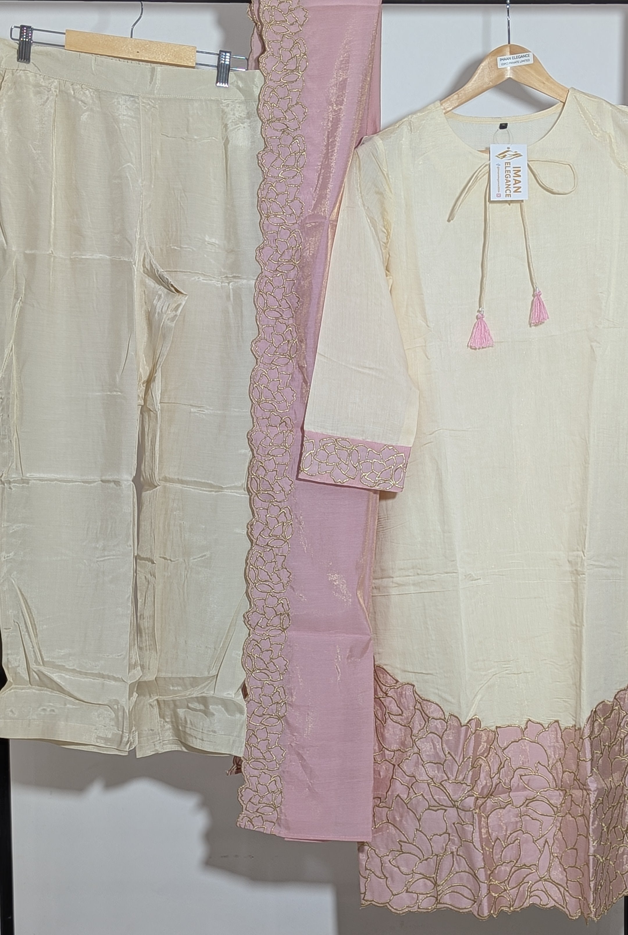 Light-colored kurta with pink lace details and matching pants on a rack.