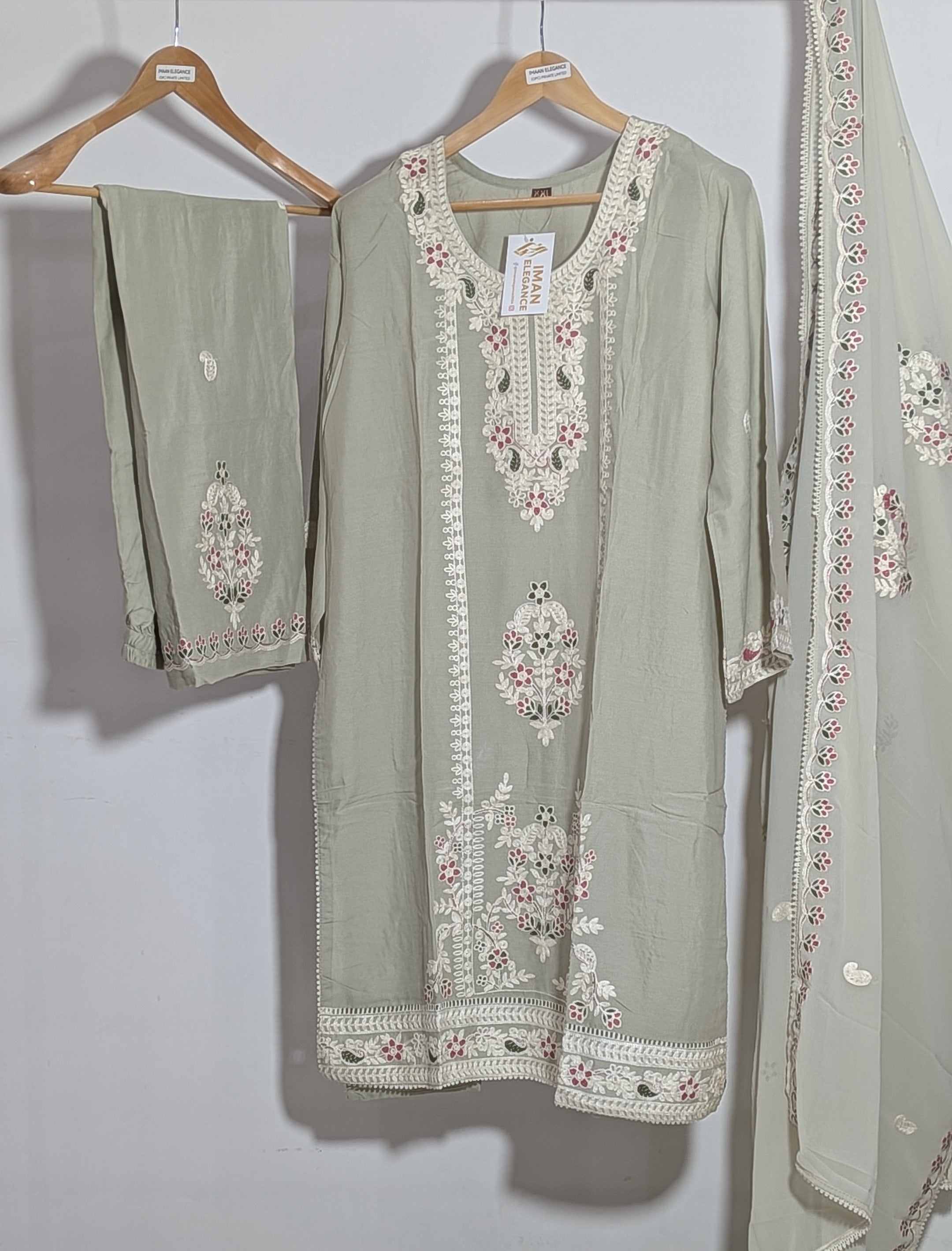 Light green embroidered traditional outfit with dupatta on a hanger against a white wall.