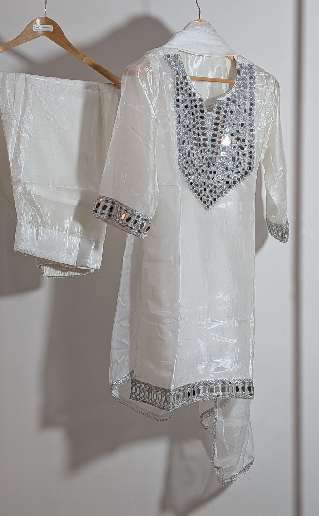 White embroidered kurta with matching pants on a hanger against a white wall.
