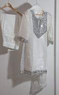 White embroidered kurta with matching pants on a hanger against a white wall.