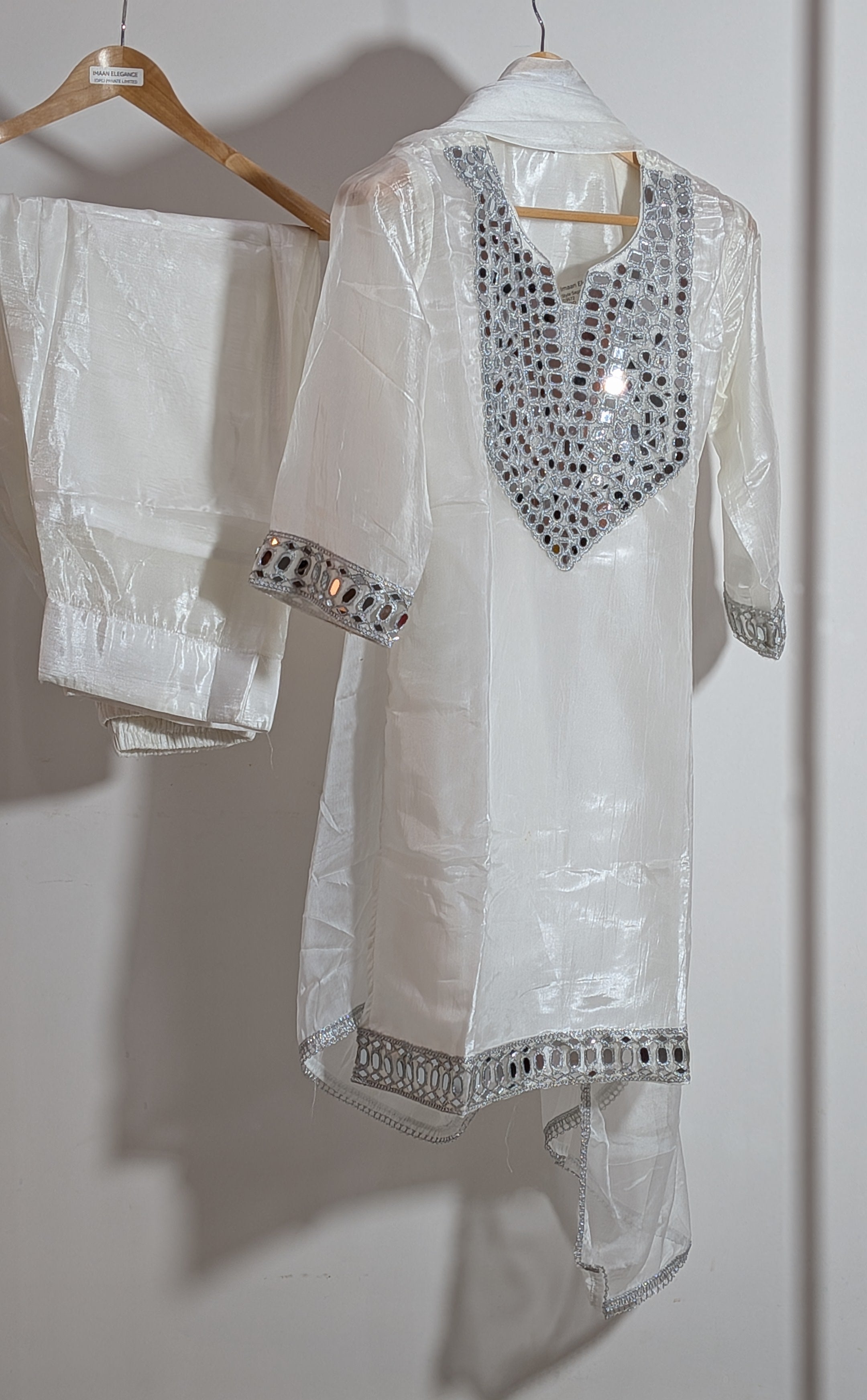 White embroidered kurta with matching pants on a hanger against a white wall.
