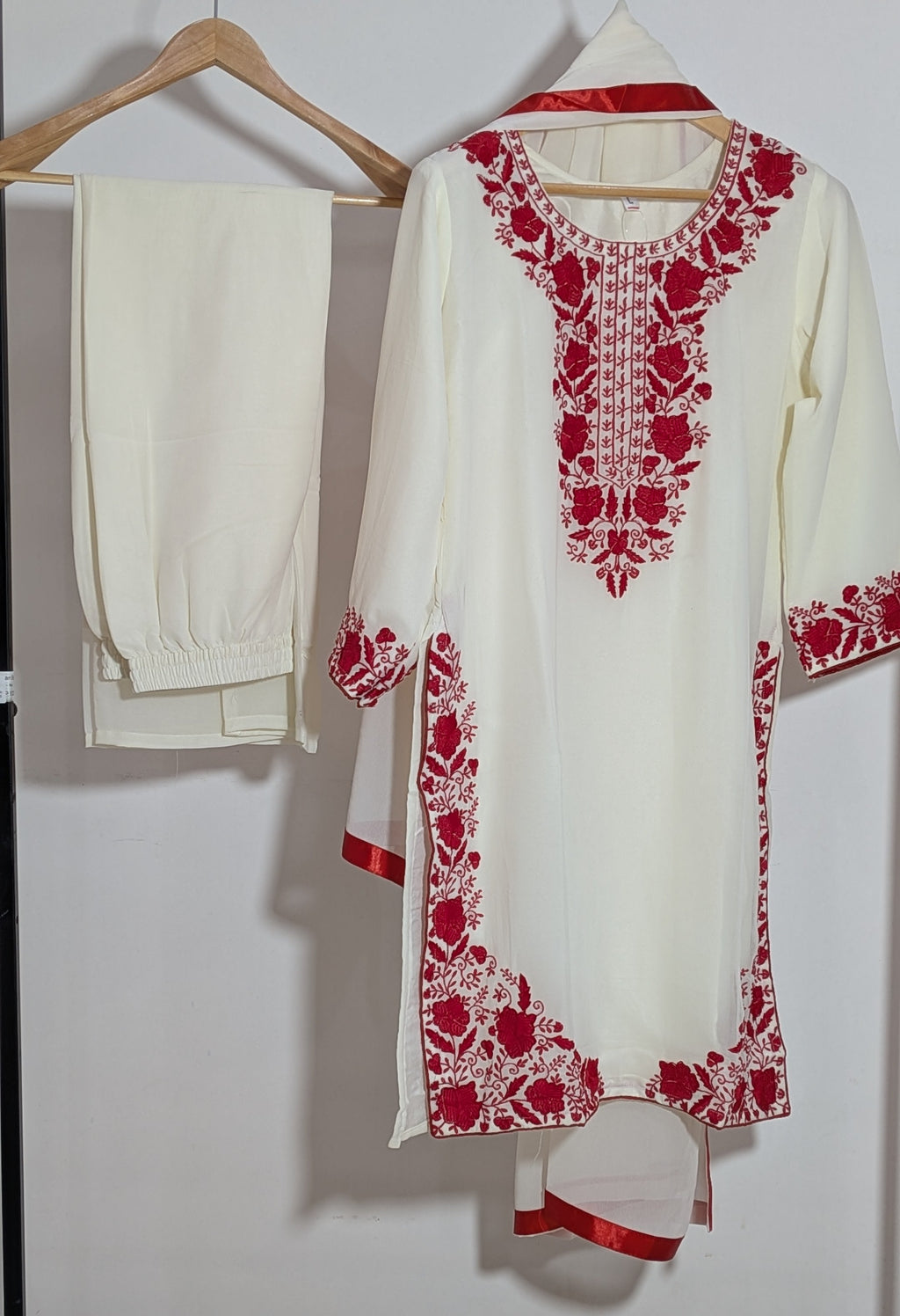 White outfit with red embroidery on a hanger against a white background