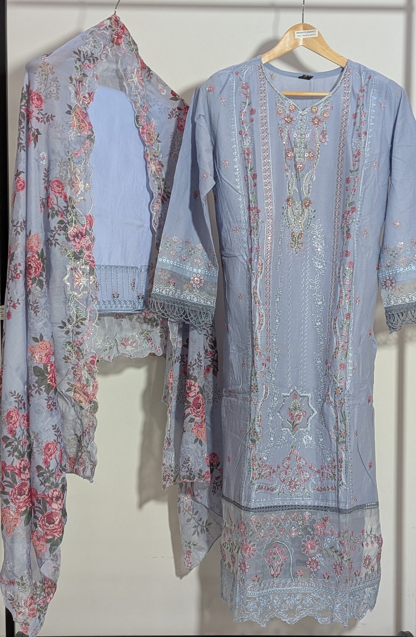 Two floral-patterned outfits hanging on a rack against a white background