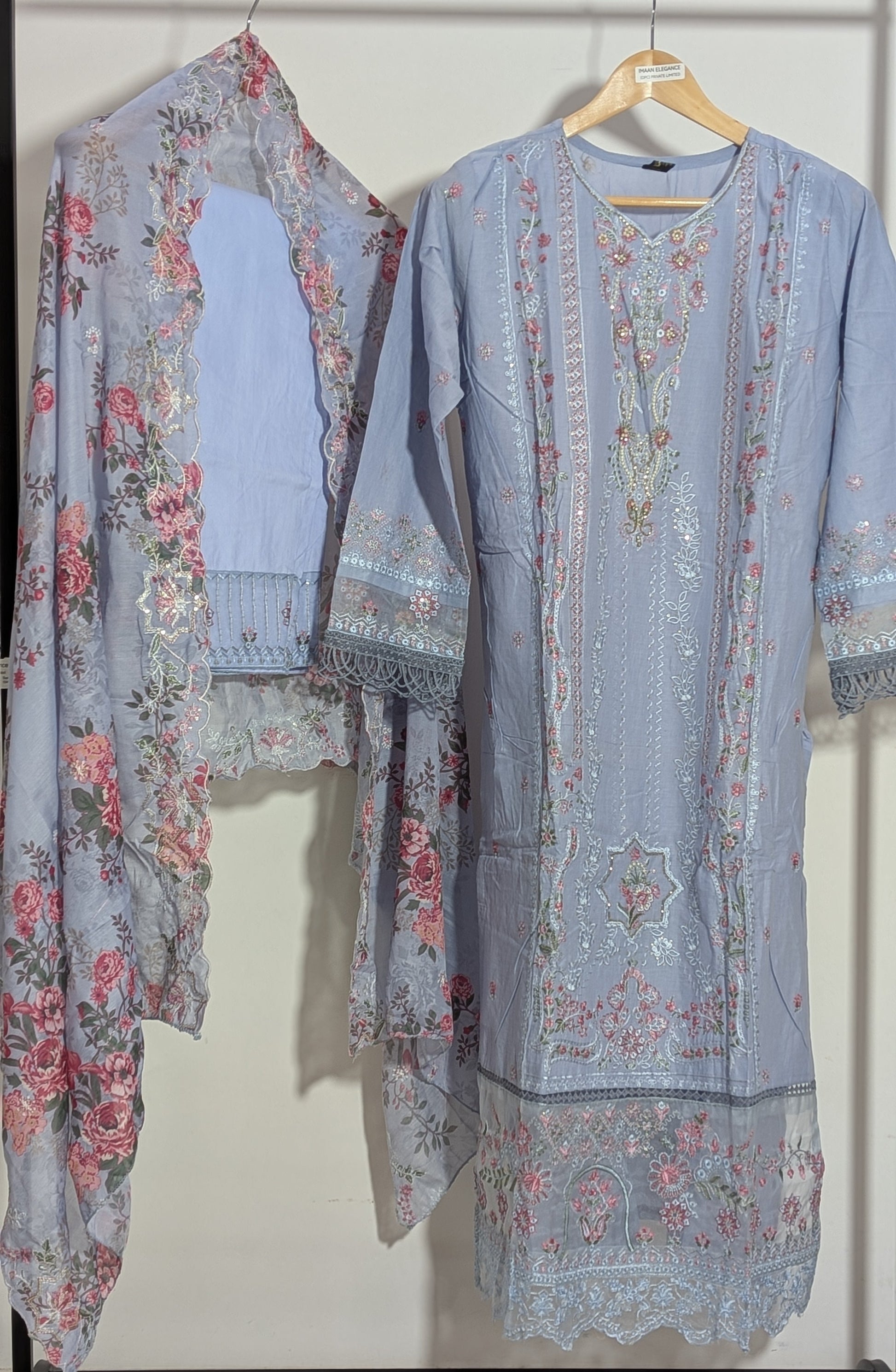 Two floral-patterned outfits hanging on a rack against a white background