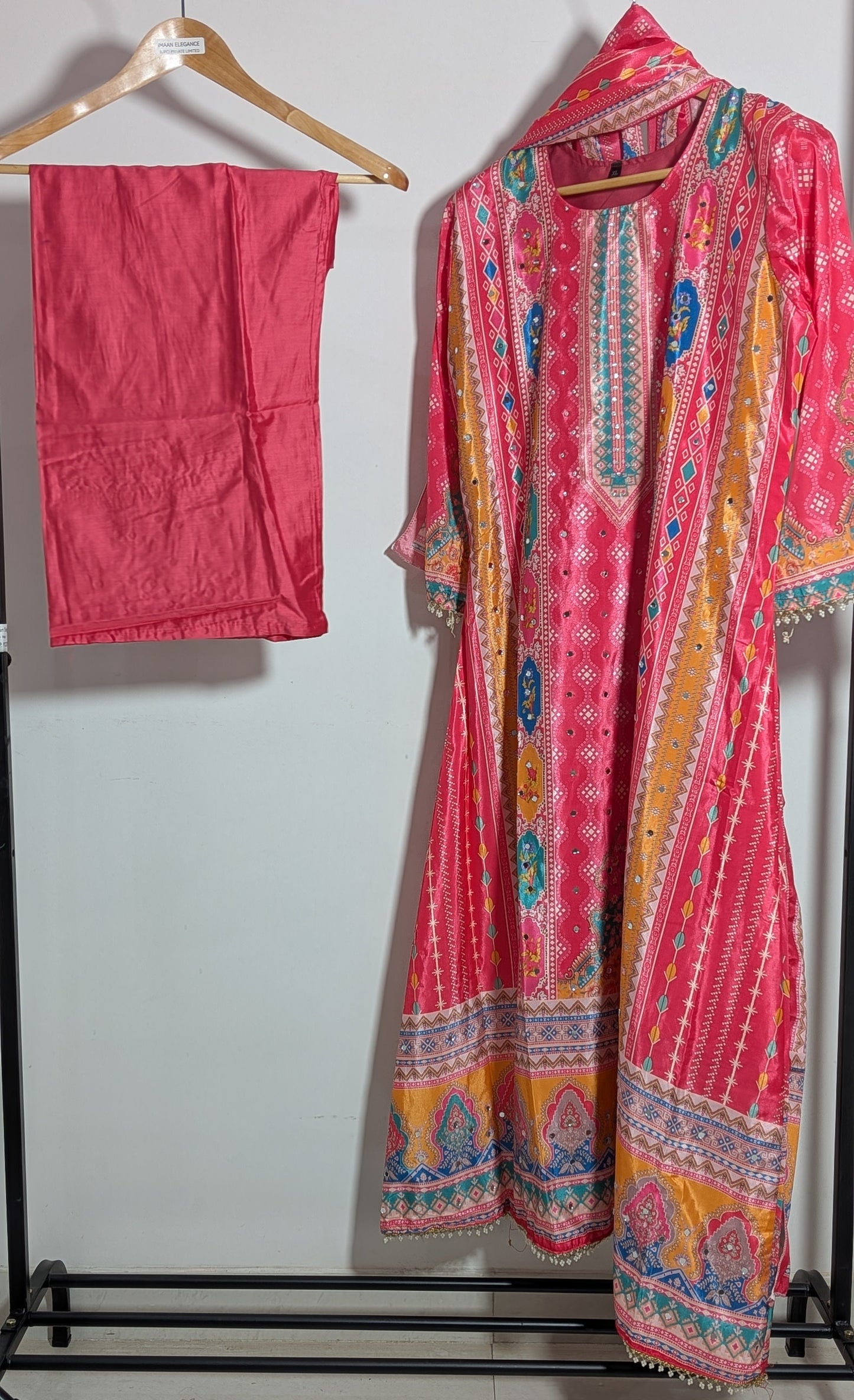 Pink embroidered traditional outfit on a rack against a white wall
