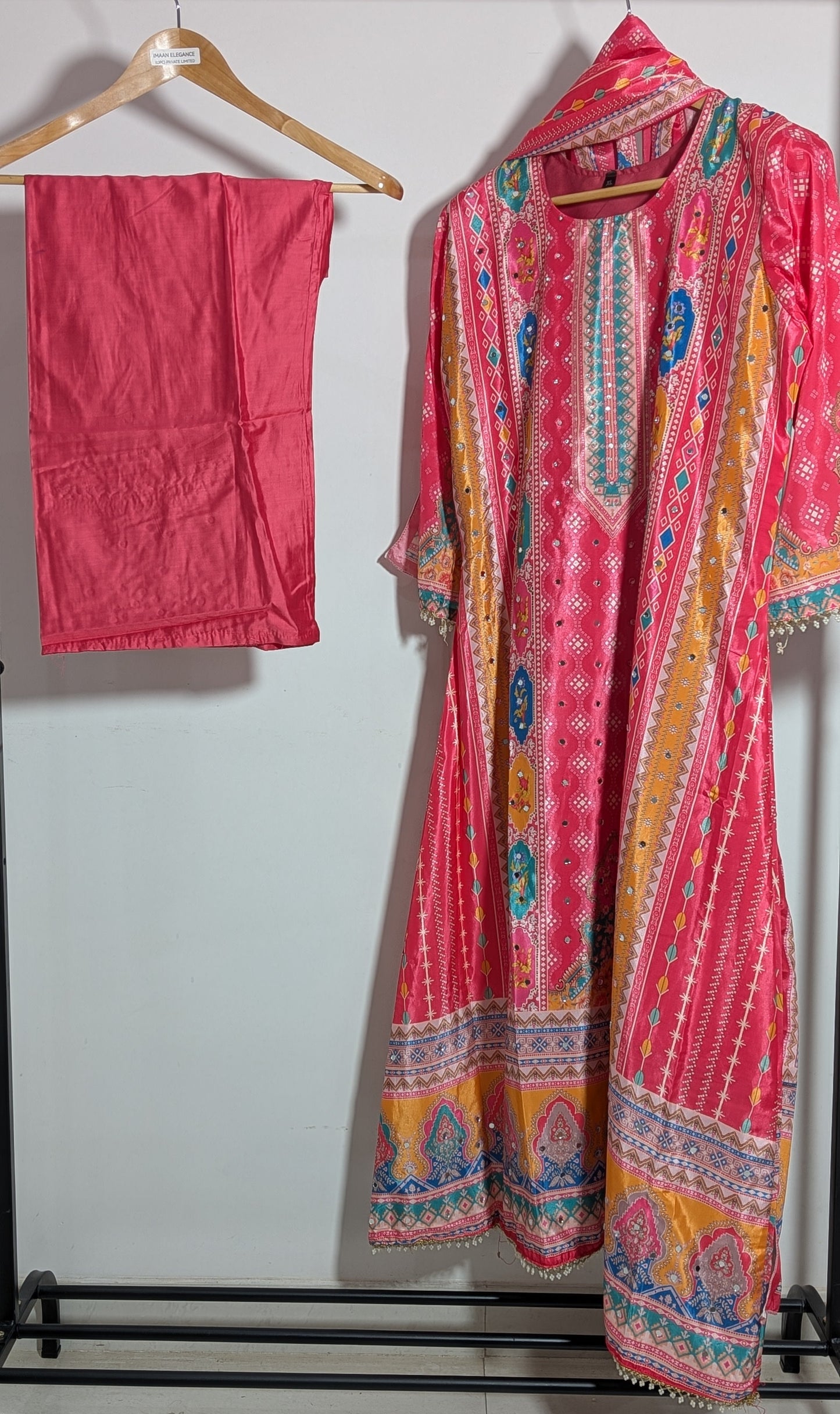 Pink embroidered traditional outfit on a hanger against a white wall