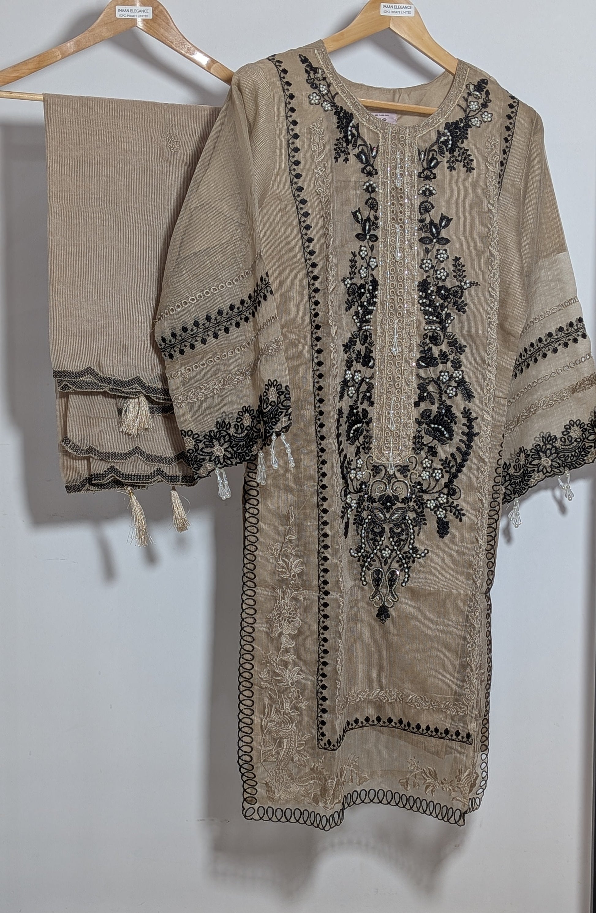 Beige embroidered dress with black patterns on a hanger against a white background